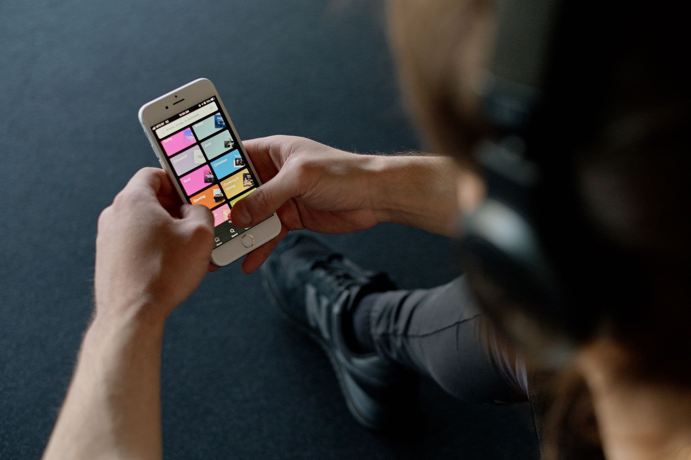 Person in headphones holding a phone that shows a grid of playlist covers