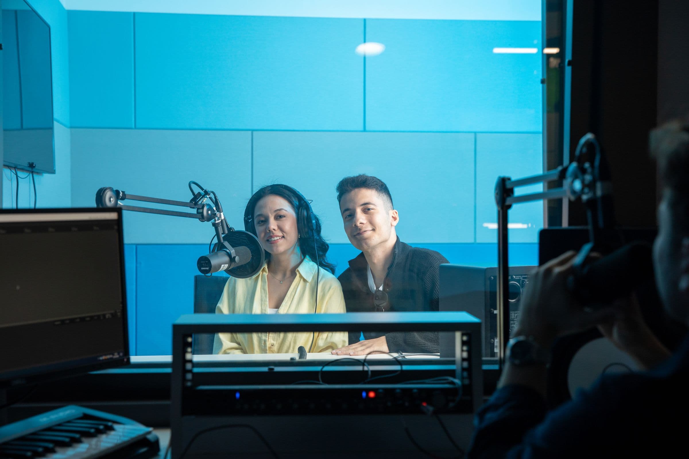 Two radio hosts talking into microphones in a bright broadcast studio