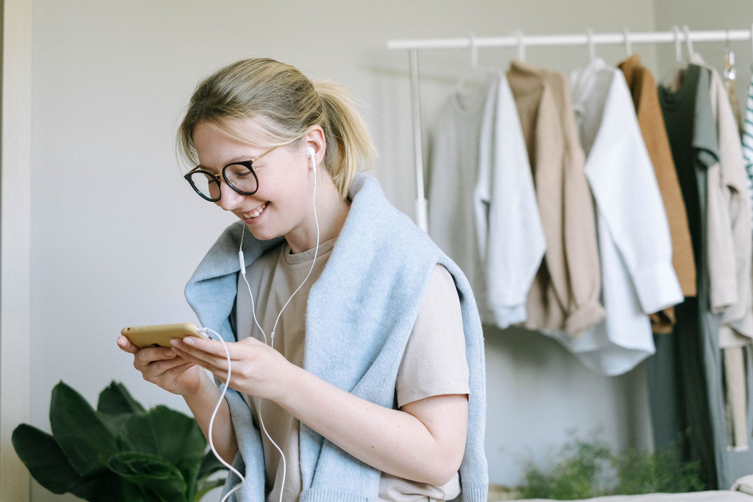 Young woman in glasses smiling at her phone while listening through earphones