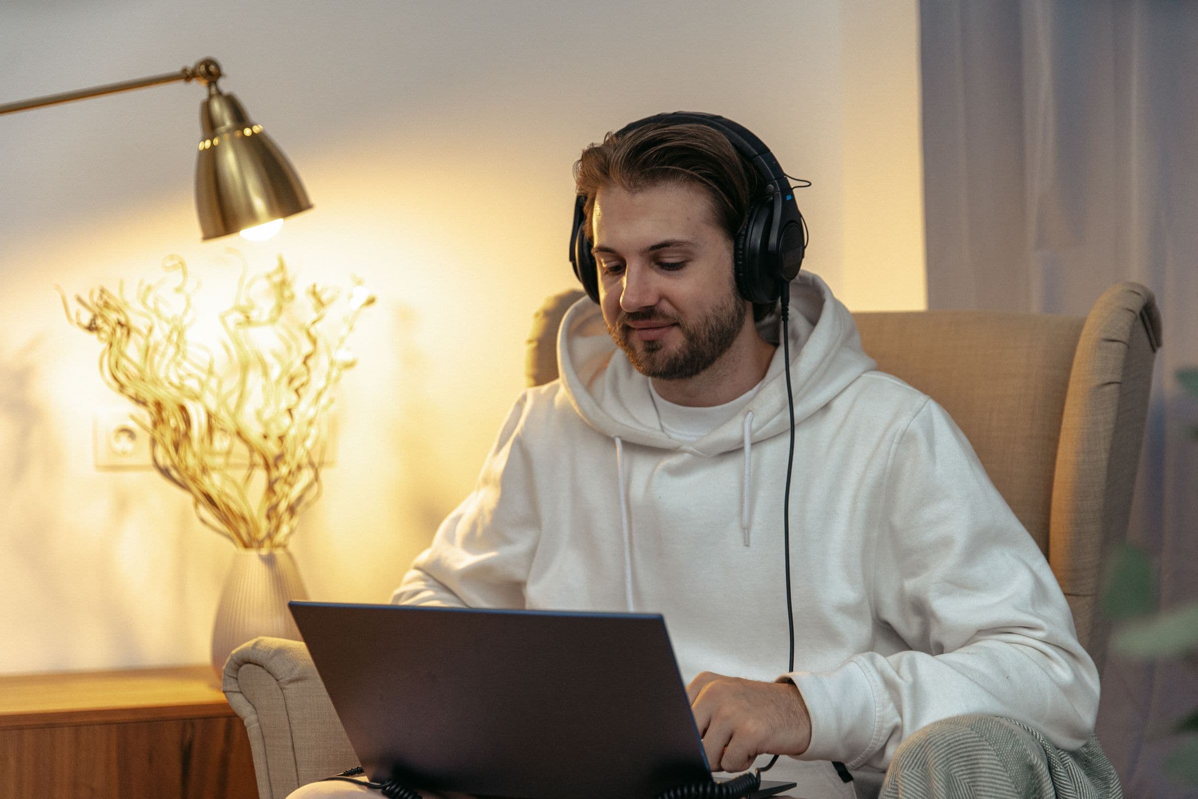 Man in headphones and a hoodie working on a laptop in an armchair