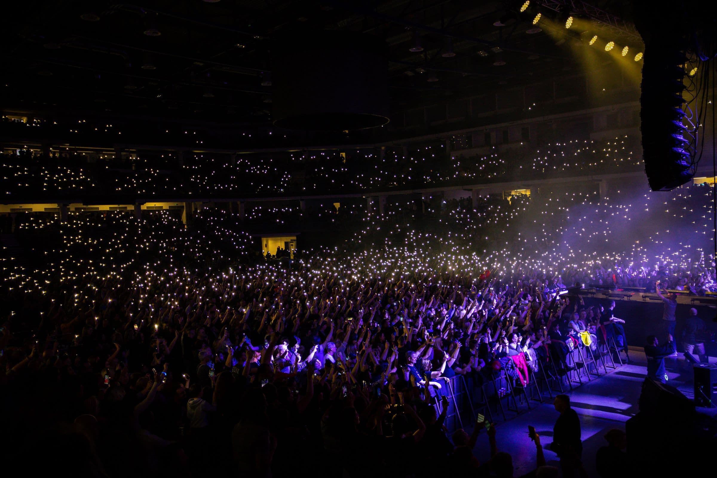 Packed arena audience holding up phone lights during a concert