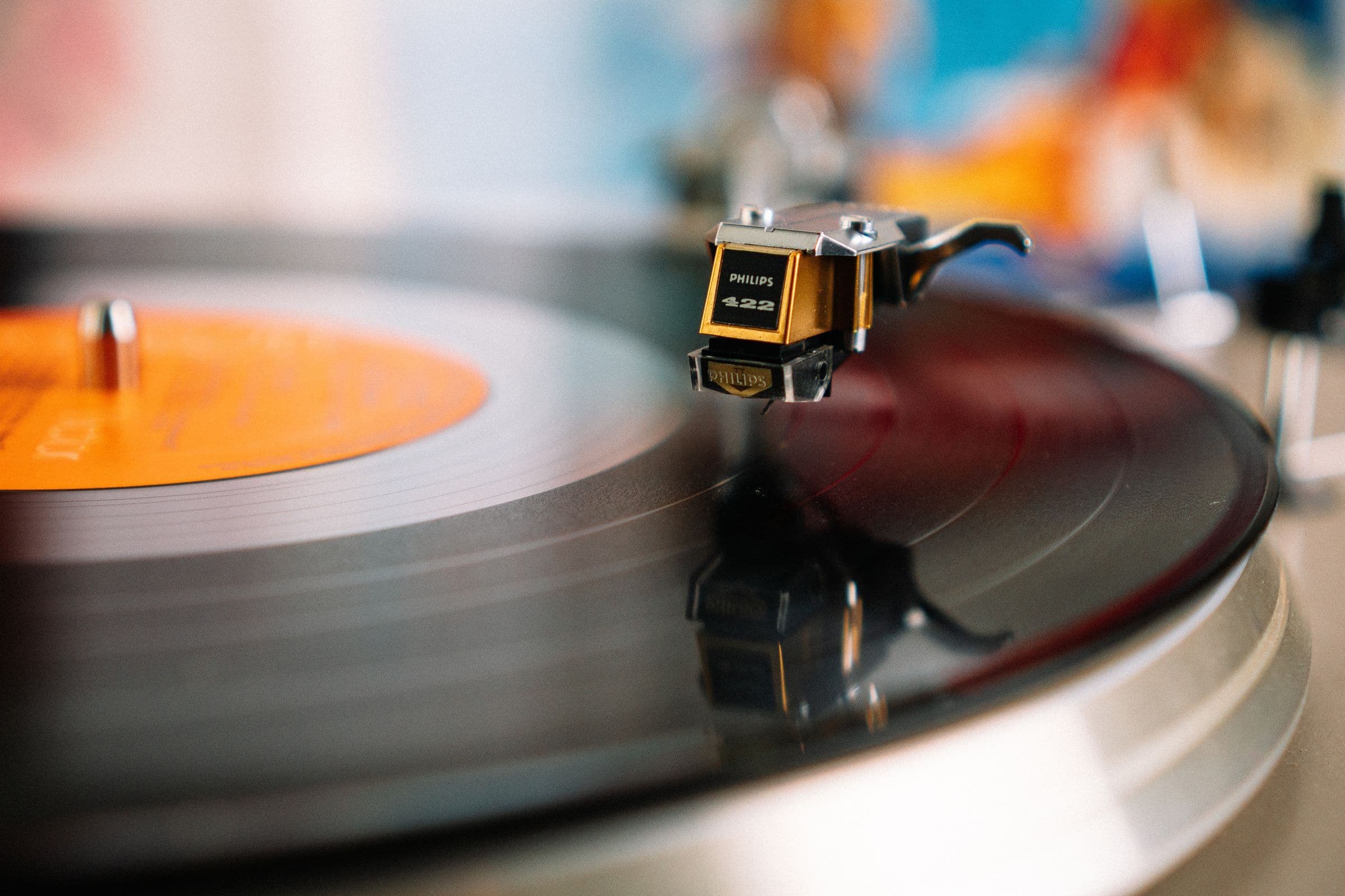 Turntable tonearm resting on a spinning vinyl record with an orange label