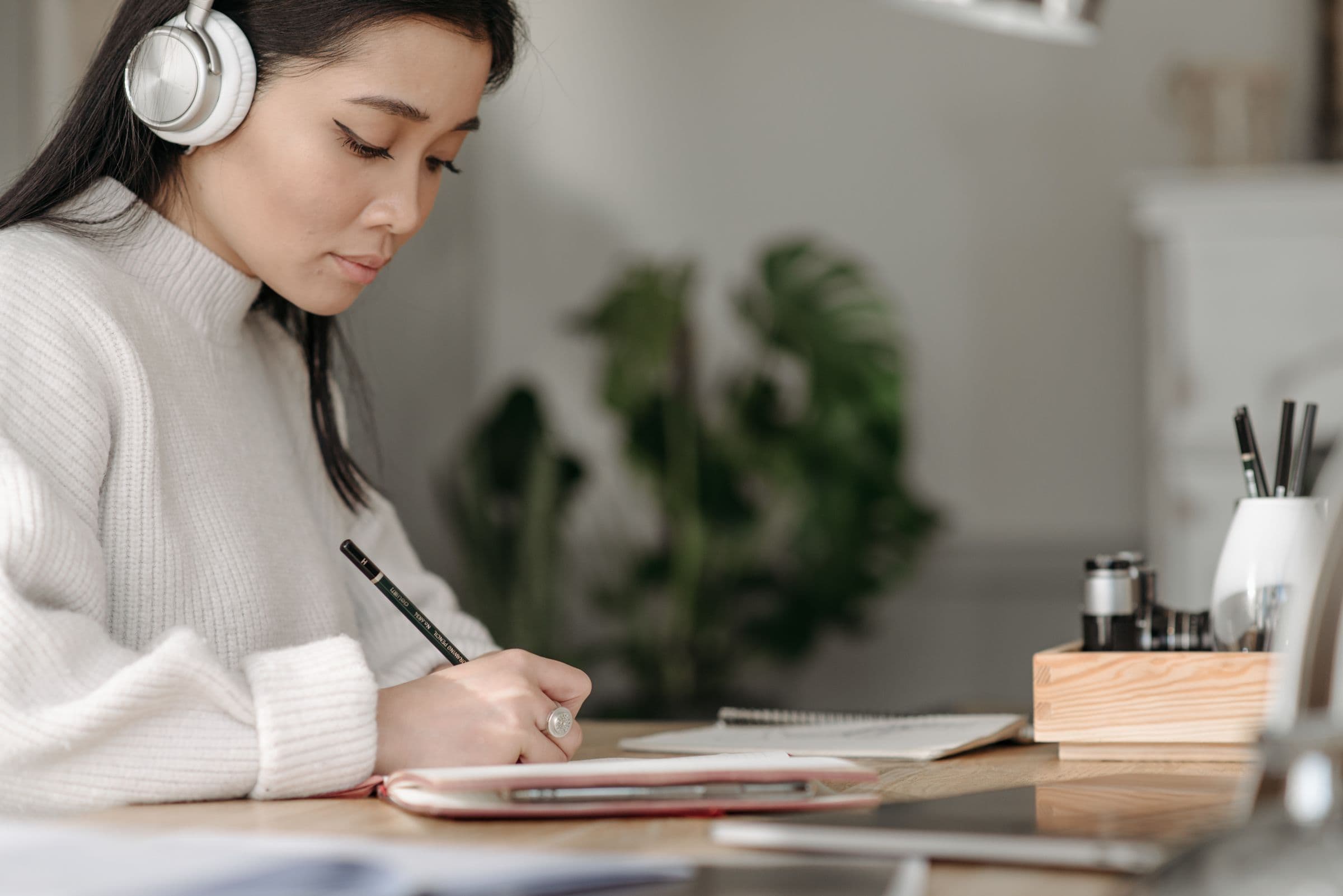 Woman in headphones writing notes at a table at home