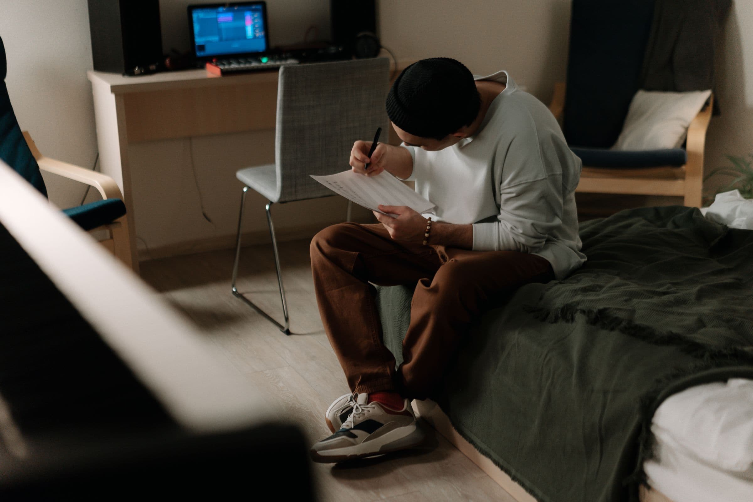 Musician writing music on paper in a small home studio next to a bed