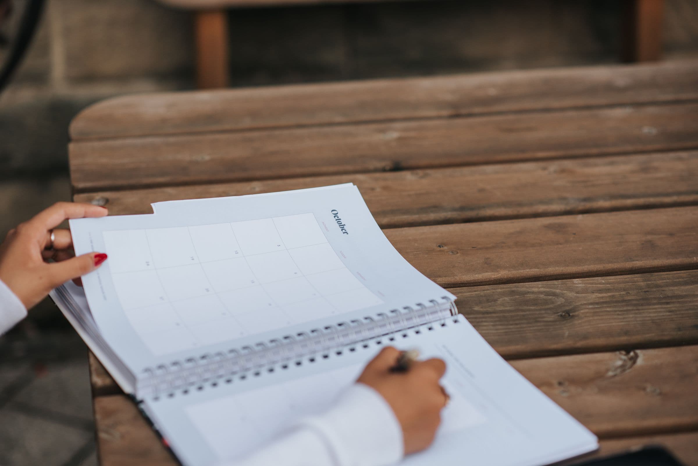 Hand writing in a spiral planner on a wooden table