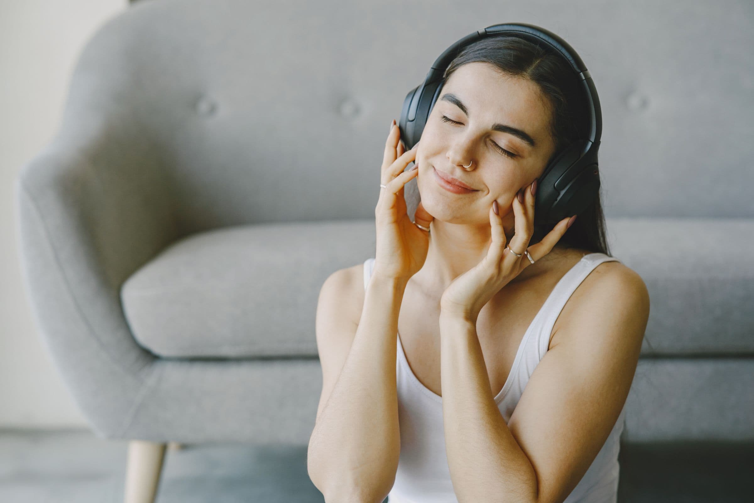 Woman with her eyes closed listening to music on wireless headphones at home
