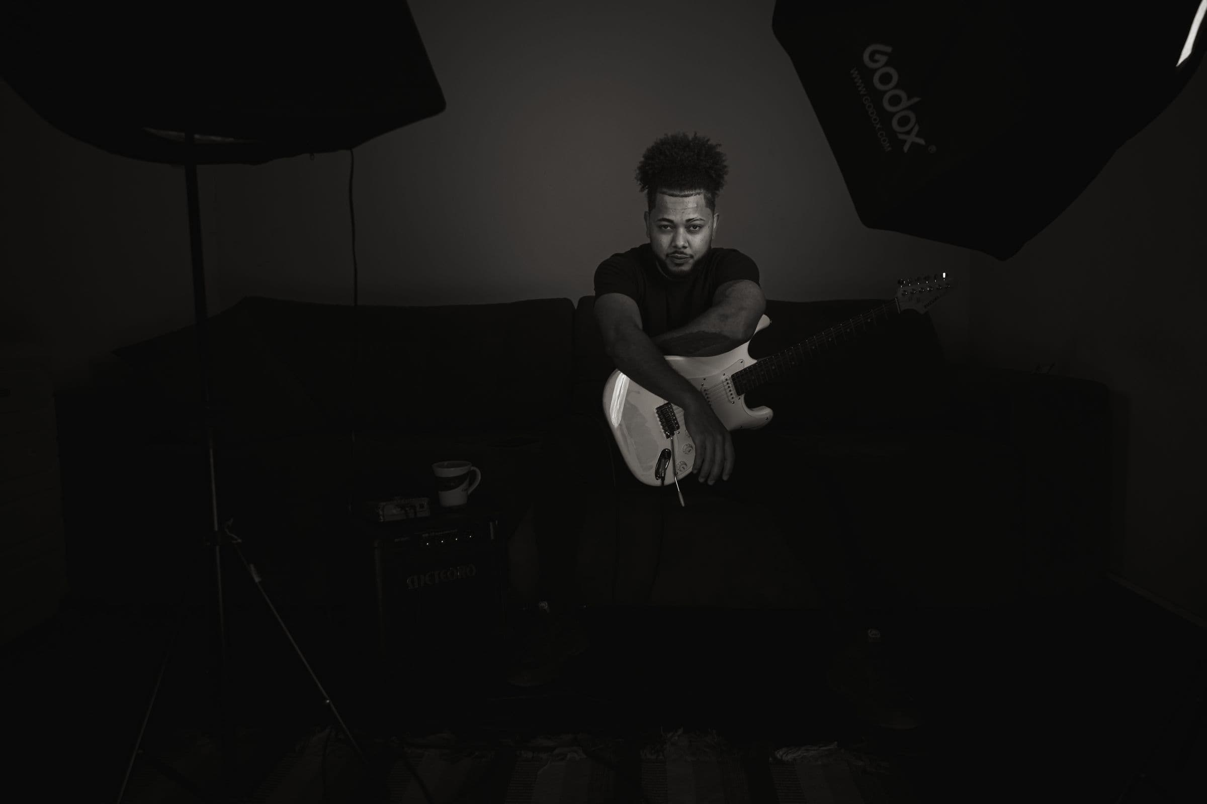 Musician holding an electric guitar alone in a dark studio