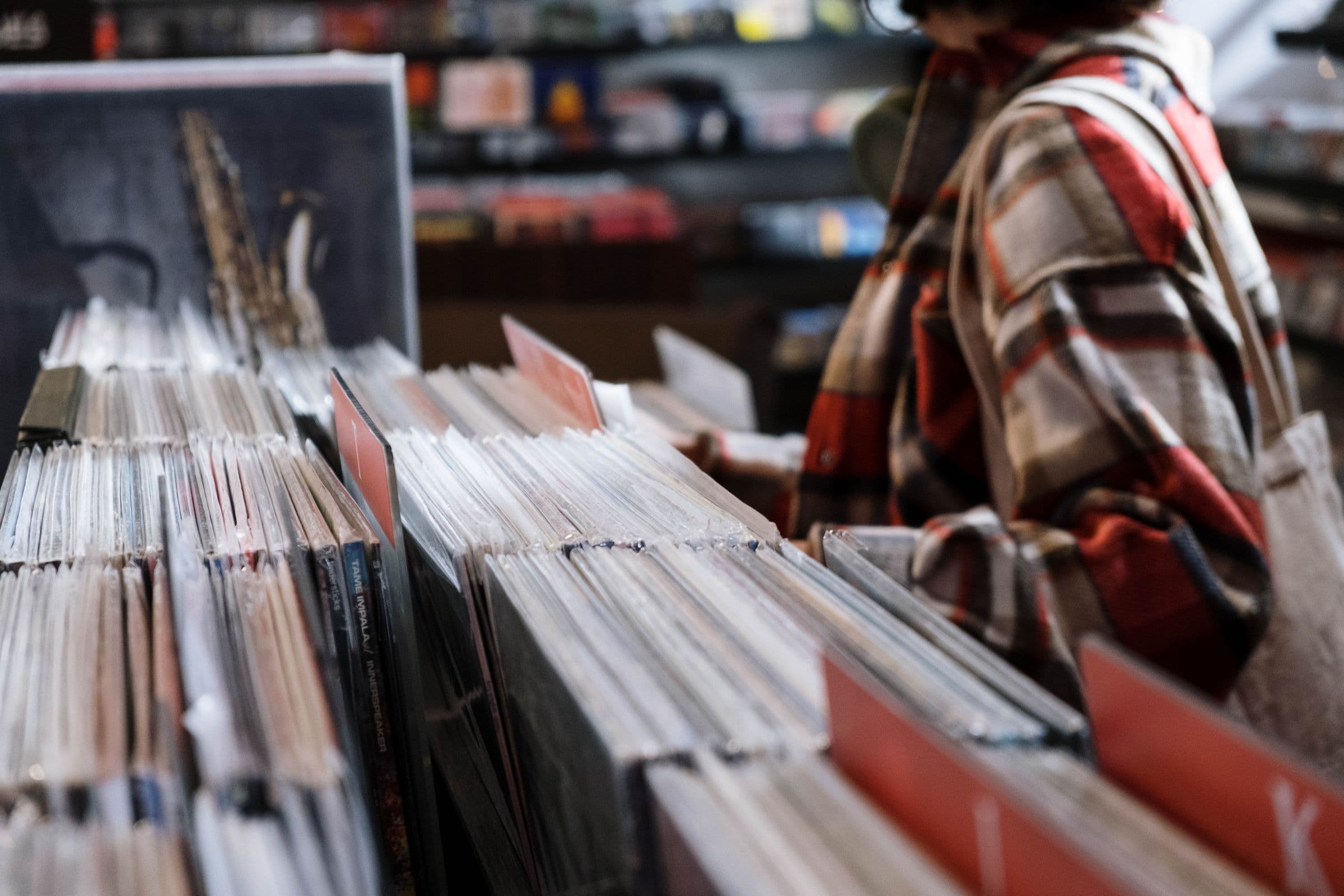 Person in a plaid shirt flipping through vinyl records in a record store