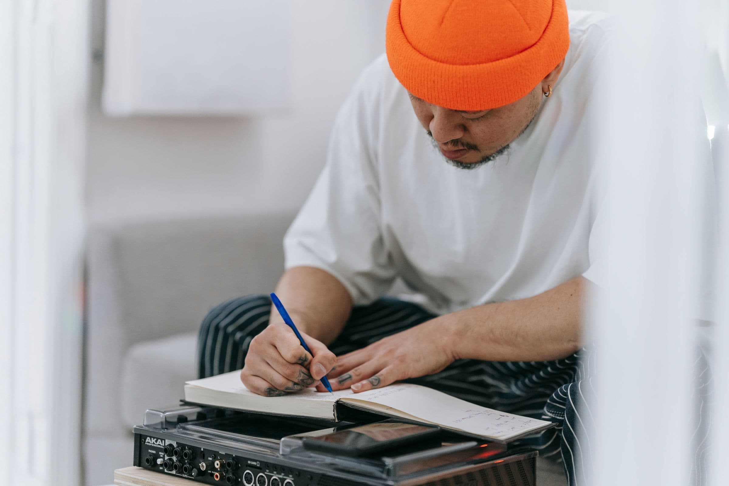 Musician in an orange beanie writing in a notebook above an audio interface