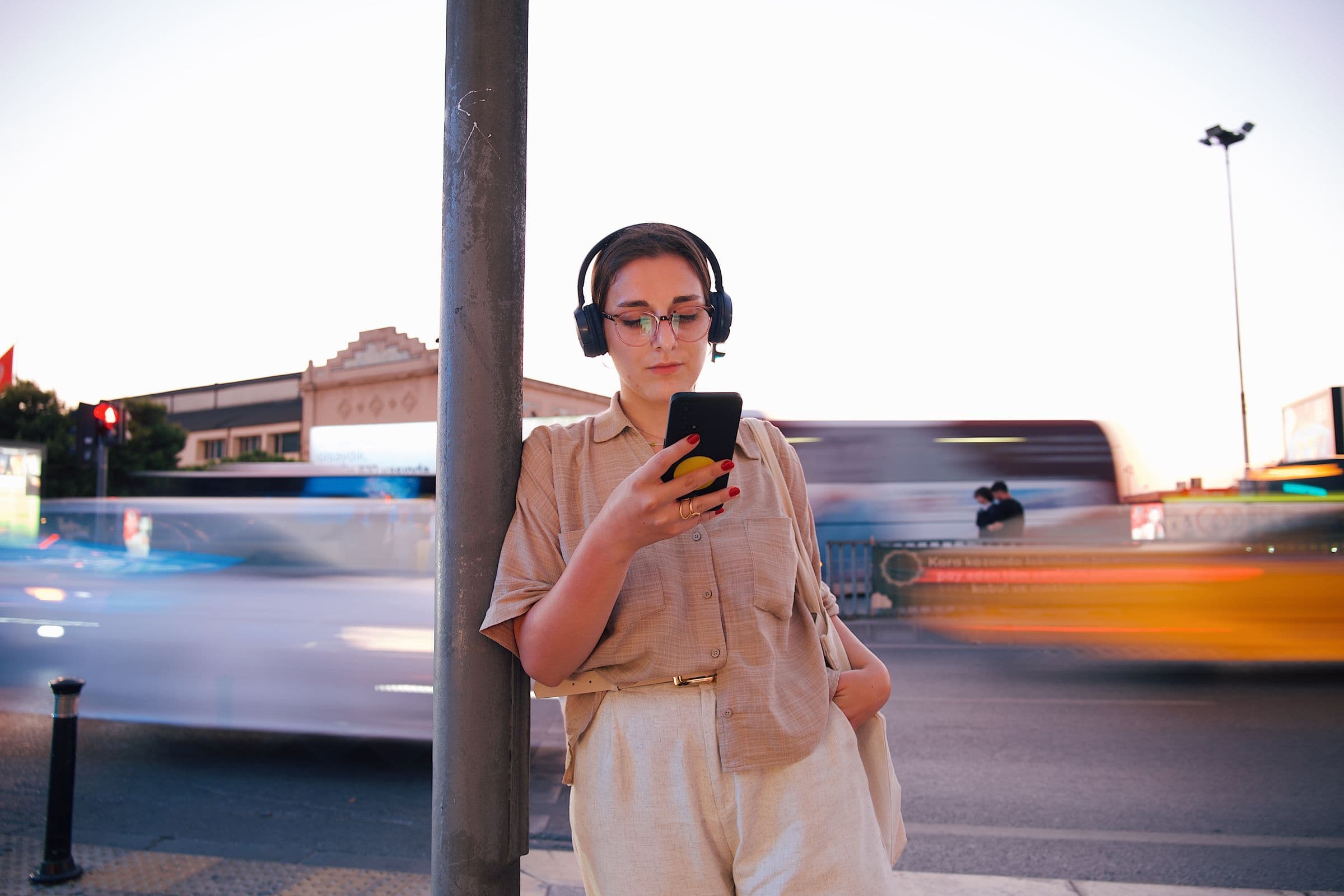 Woman in headphones looking at her phone on a city street as traffic rushes past