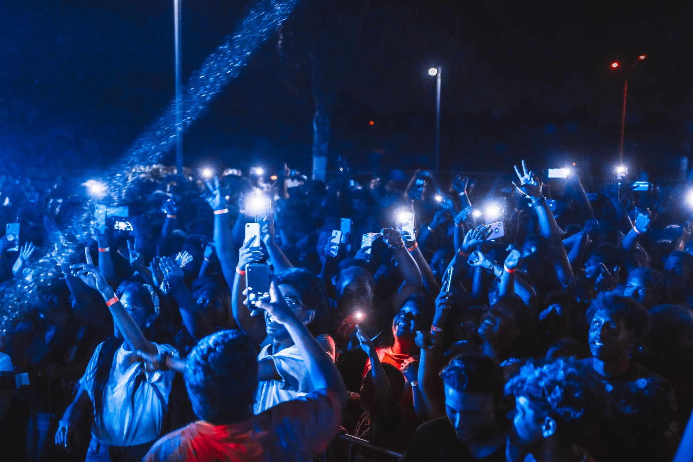 Concert crowd holding up glowing phones under blue stage lights