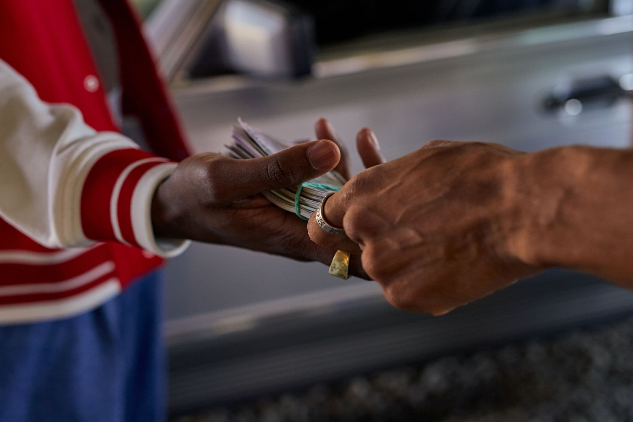 Two hands passing a folded bundle of cash beside a car