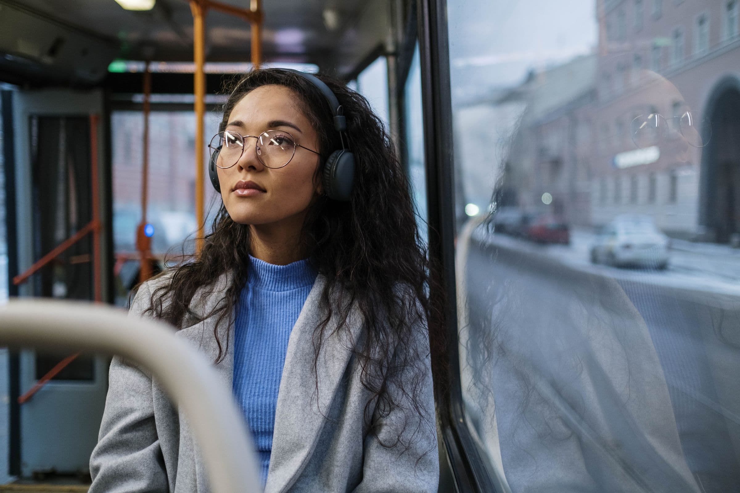 Woman in headphones and glasses riding a city bus, looking out the window
