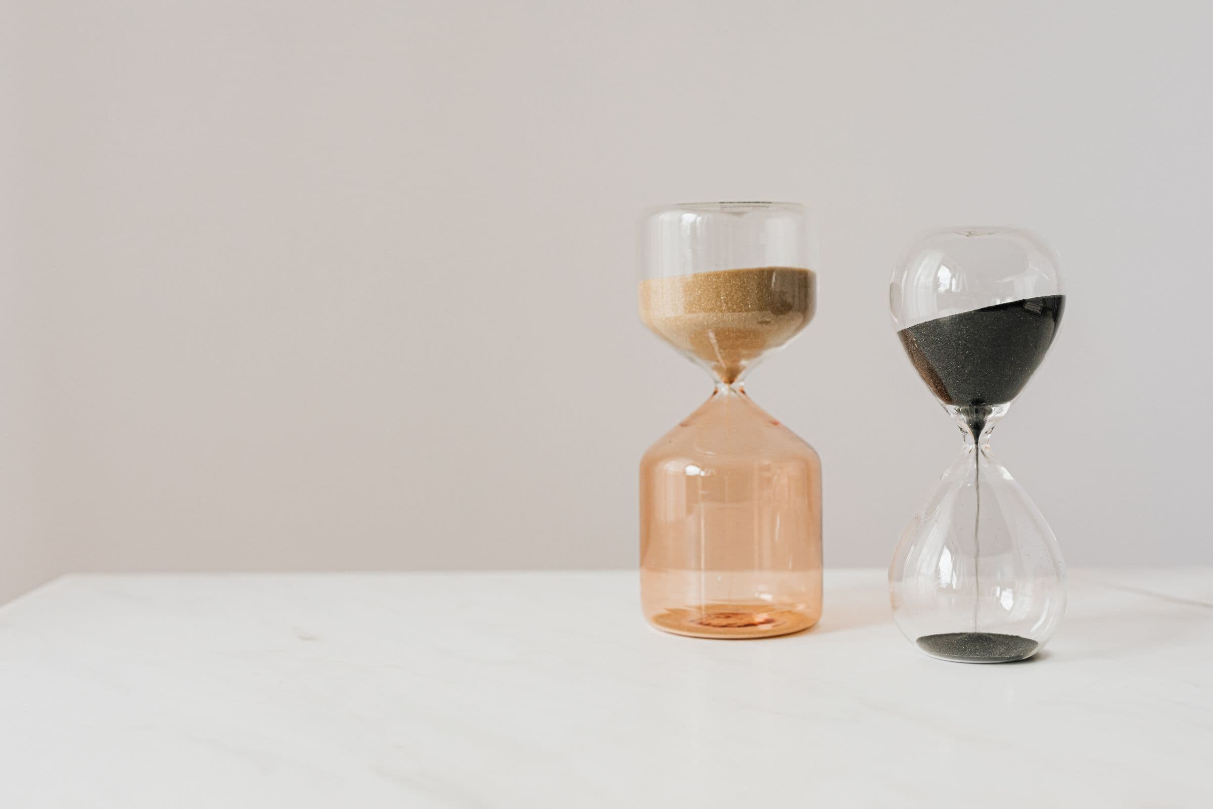 Two decorative hourglasses with beige and black sand on a white table