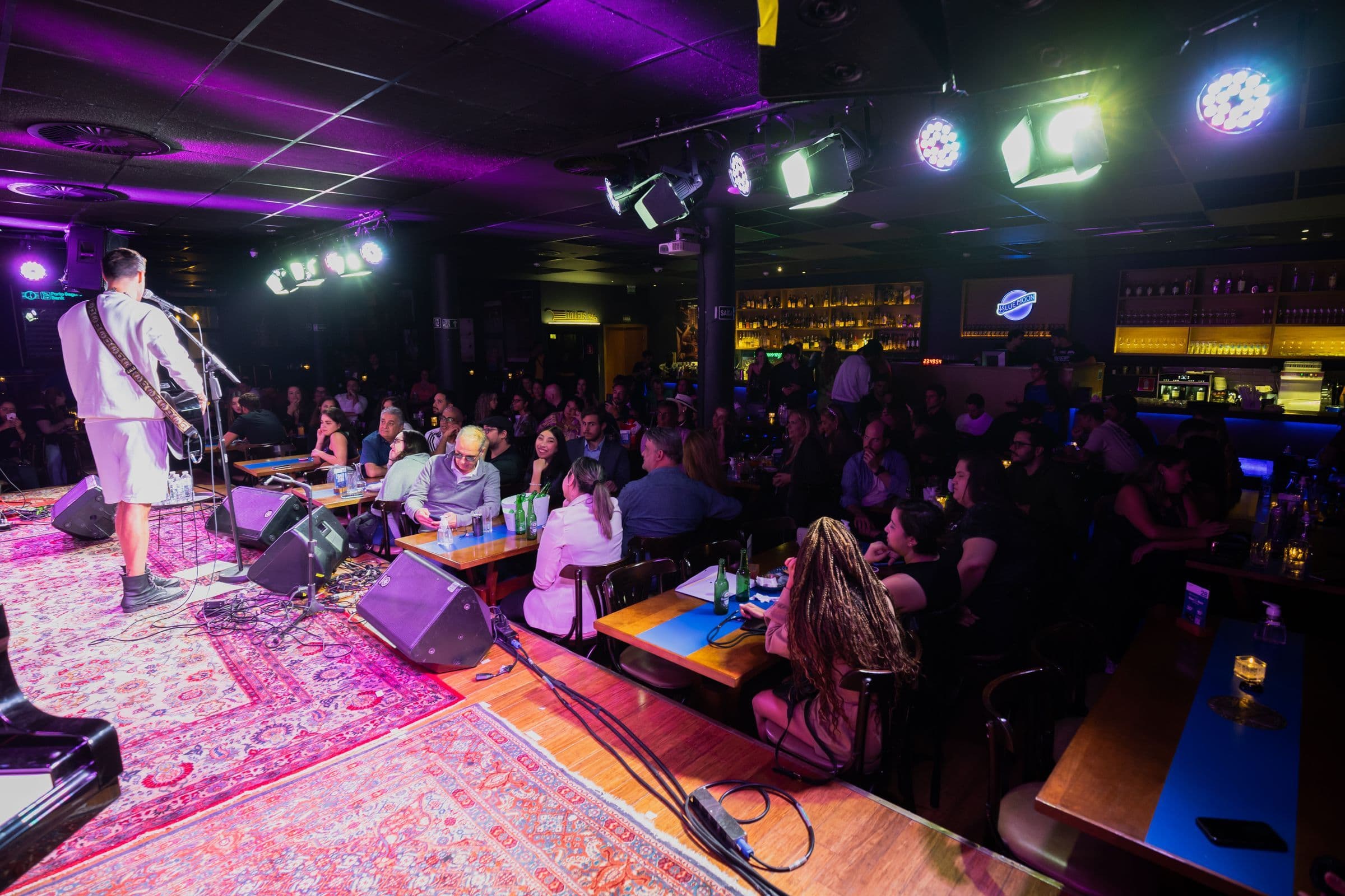 Singer with a guitar performing to a seated crowd in a small club lit in purple