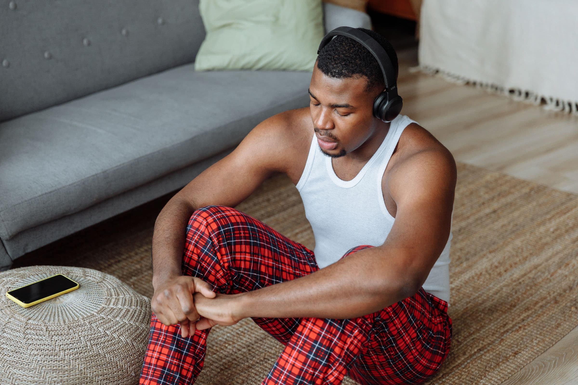 Man in headphones sitting on a living room floor, listening with his eyes down