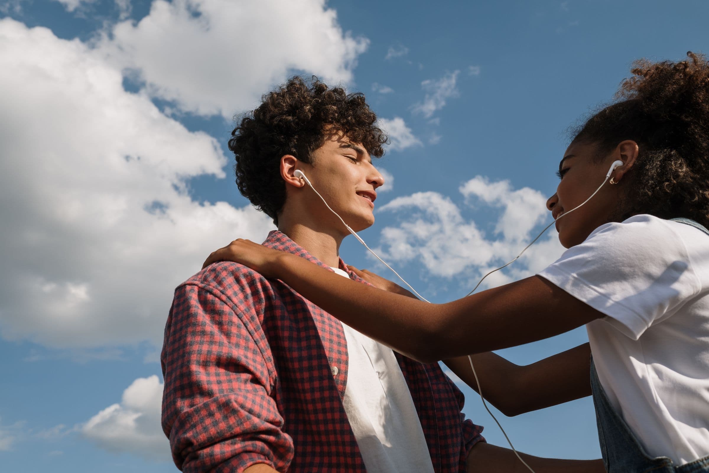 Two teenagers sharing a pair of earphones under a blue sky