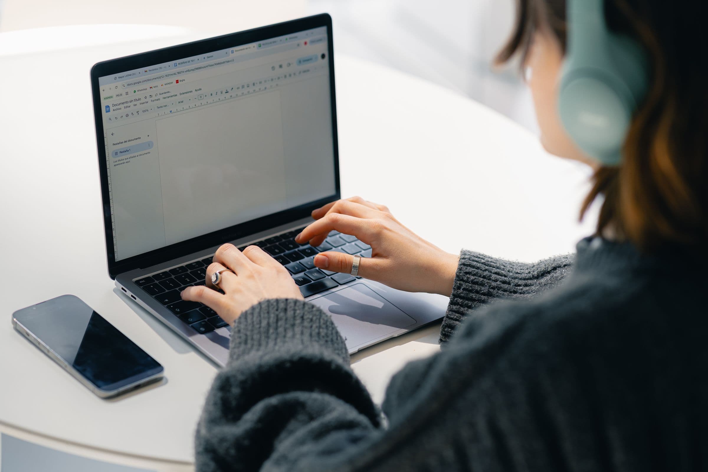 Person in headphones typing an email on a laptop, with a phone on the table