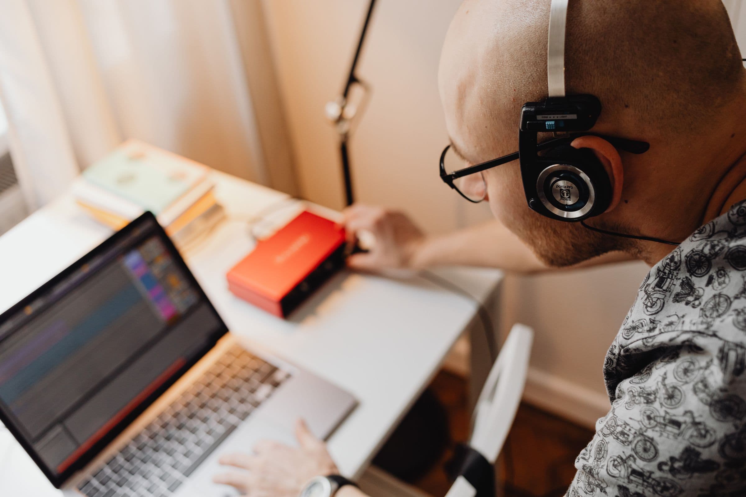Musician in headphones working on a track on a laptop, with an audio interface on the desk