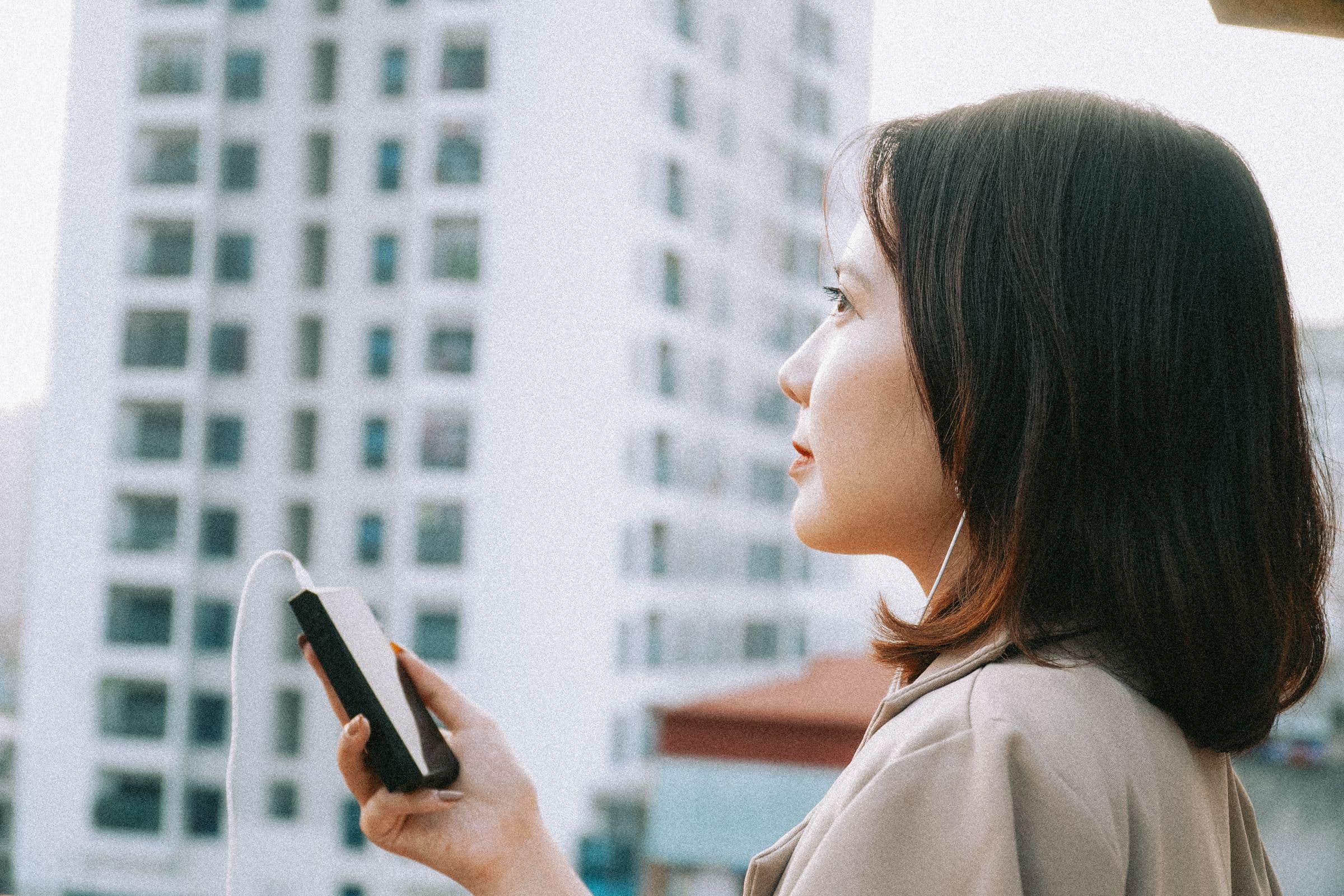 Woman with earphones holding a phone, looking out over a city
