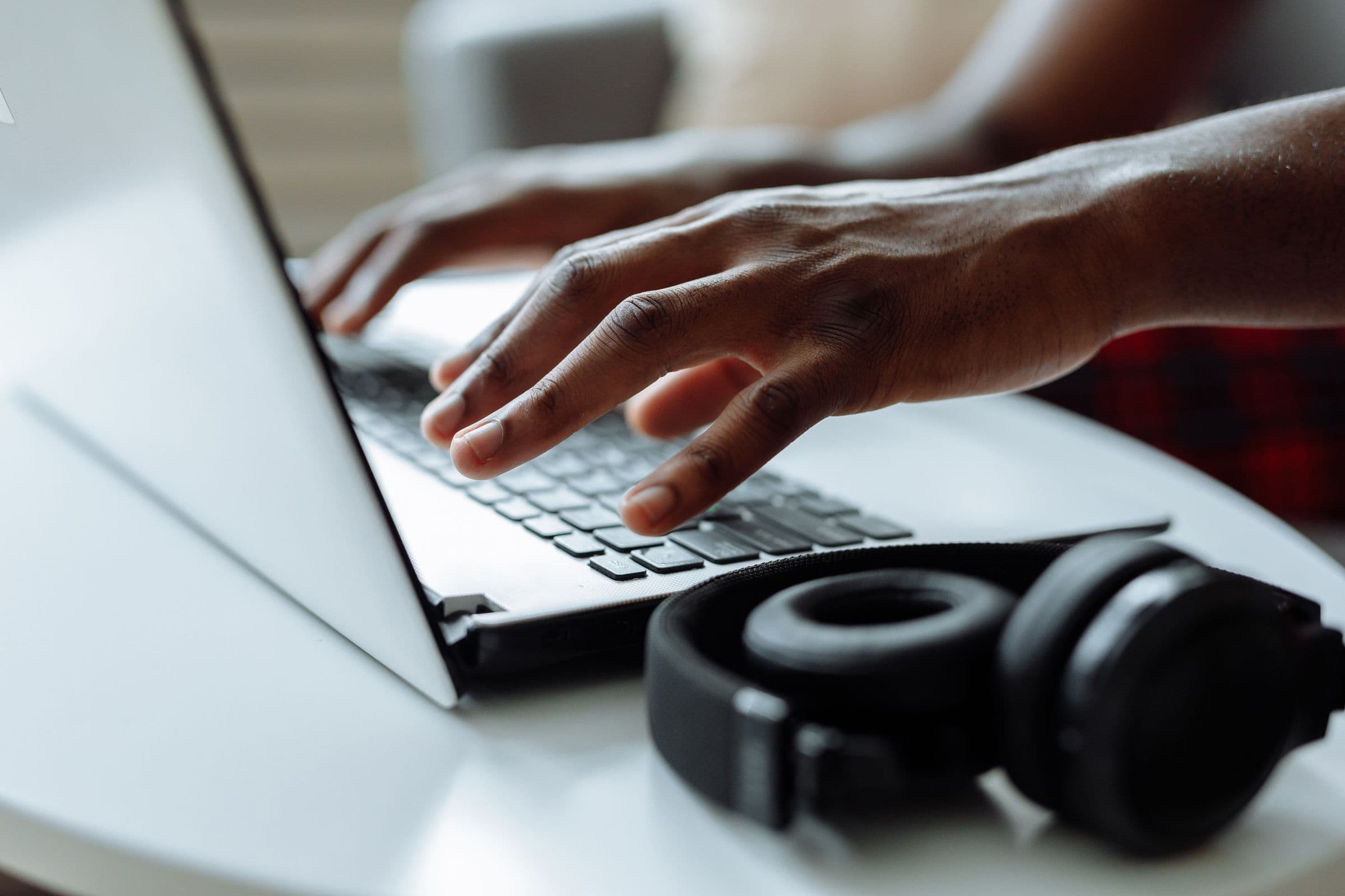 Hands typing on a laptop with black headphones resting beside it on a white table