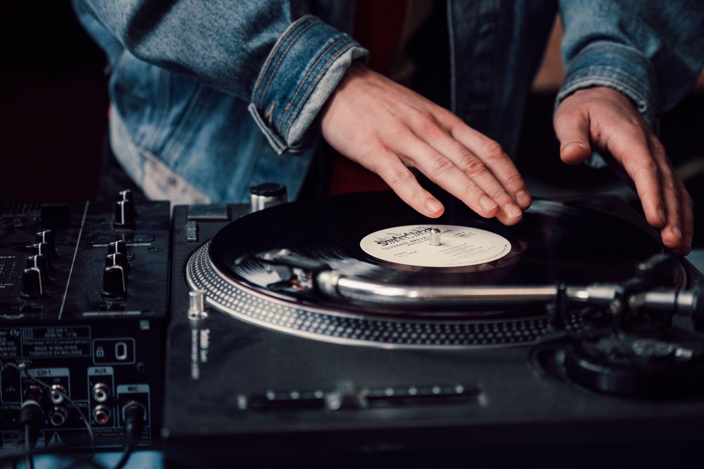 DJ's hands on a vinyl turntable next to a mixer