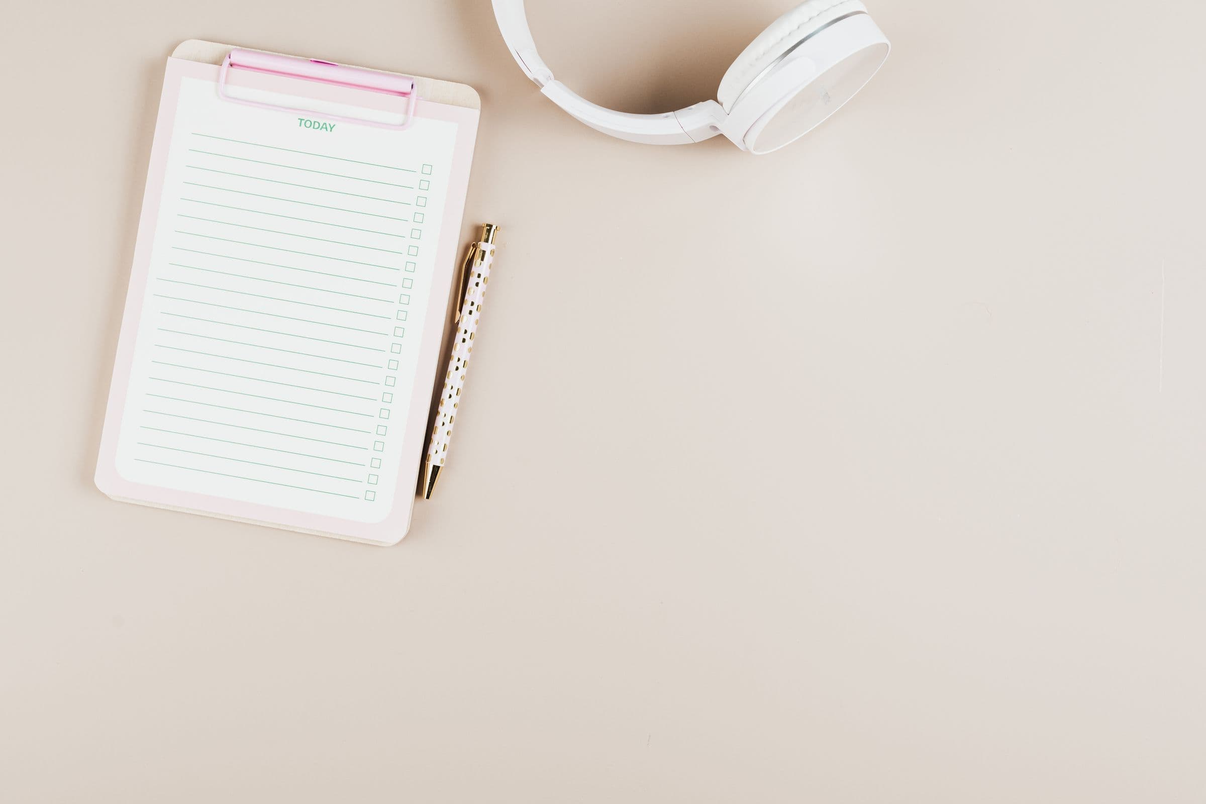 Blank checklist on a clipboard next to a pen and white headphones