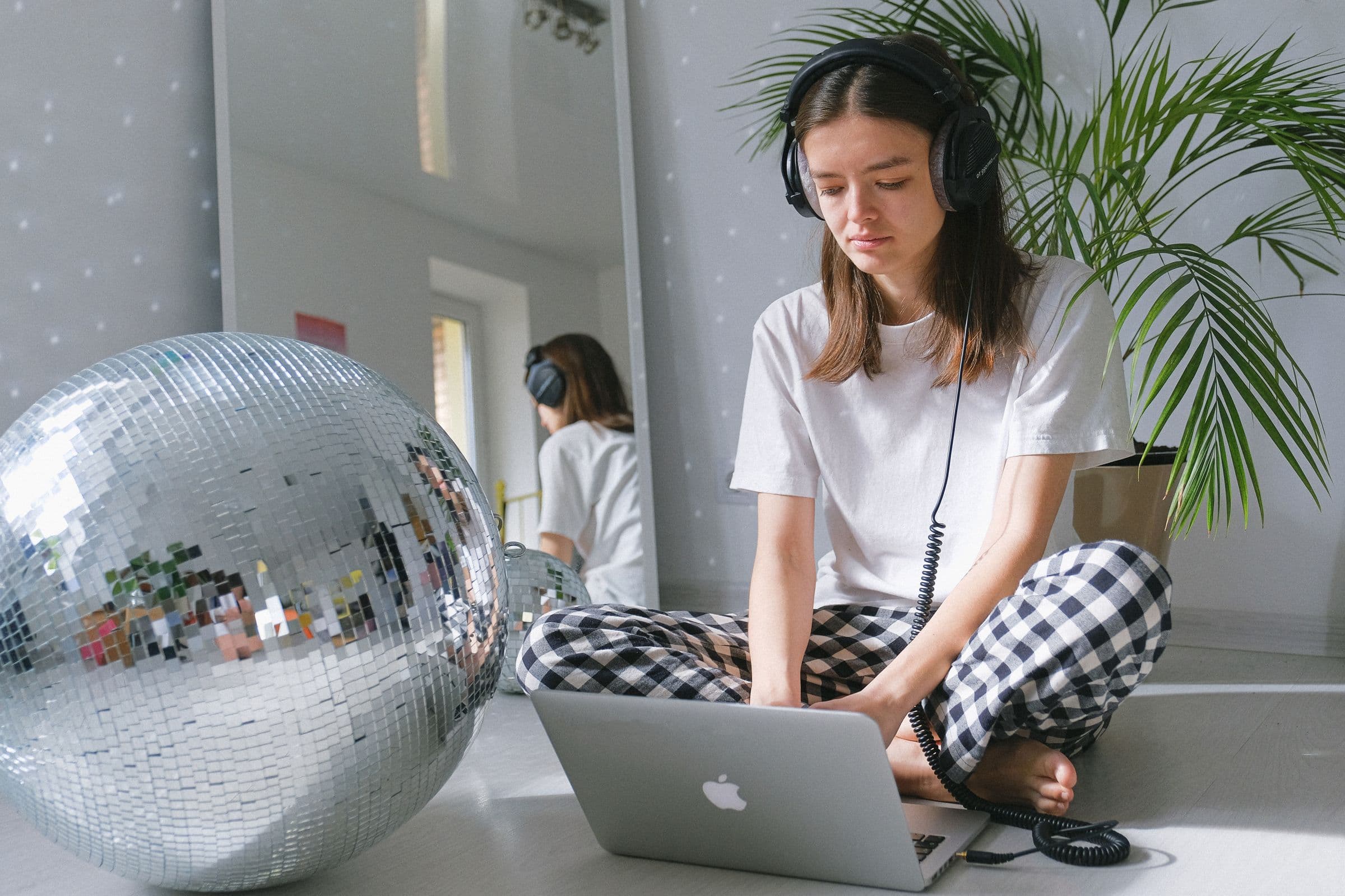 Woman in headphones choosing music on a laptop, sitting on the floor next to a disco ball