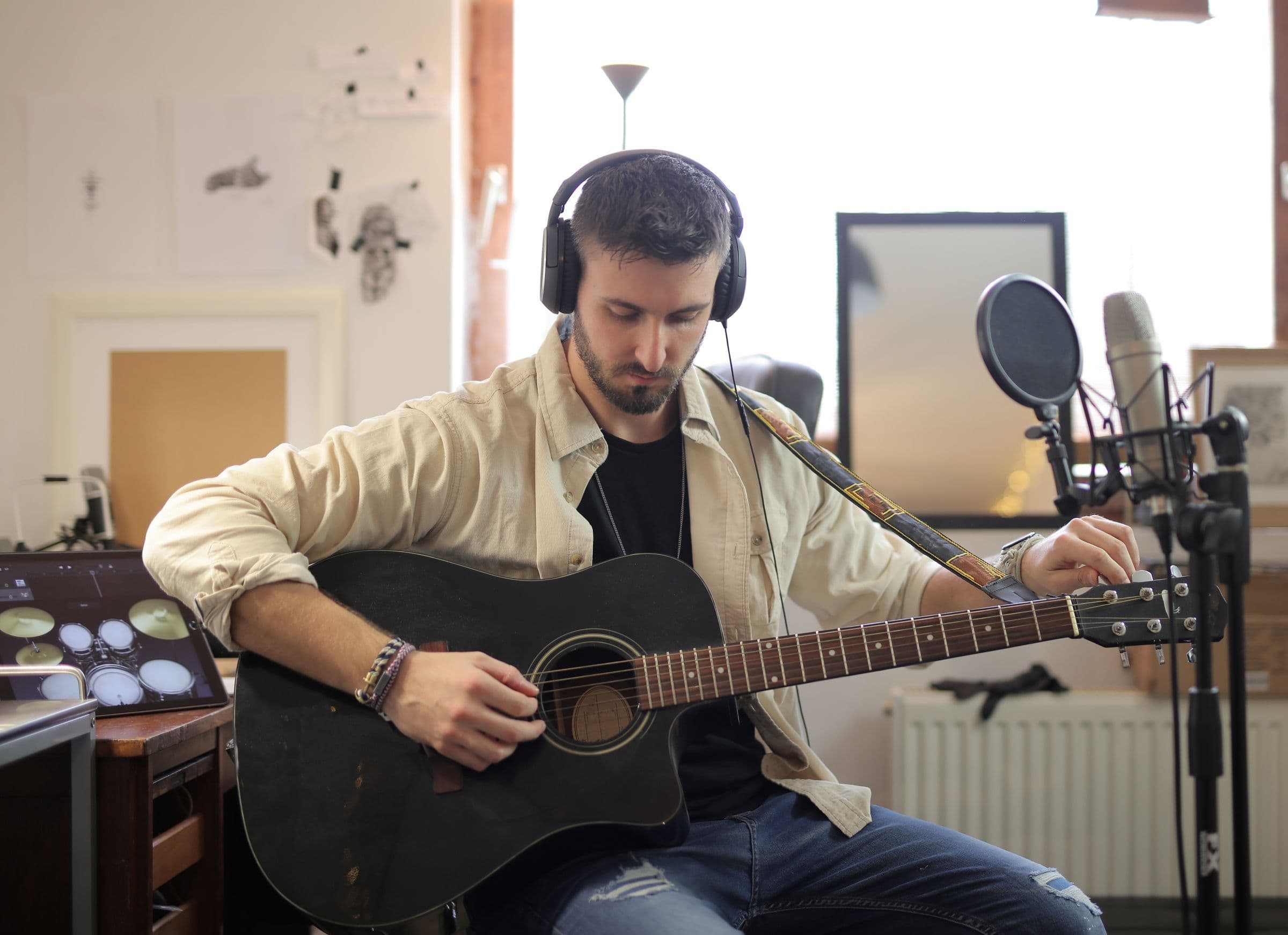 Musician in headphones playing an acoustic guitar in front of a studio microphone
