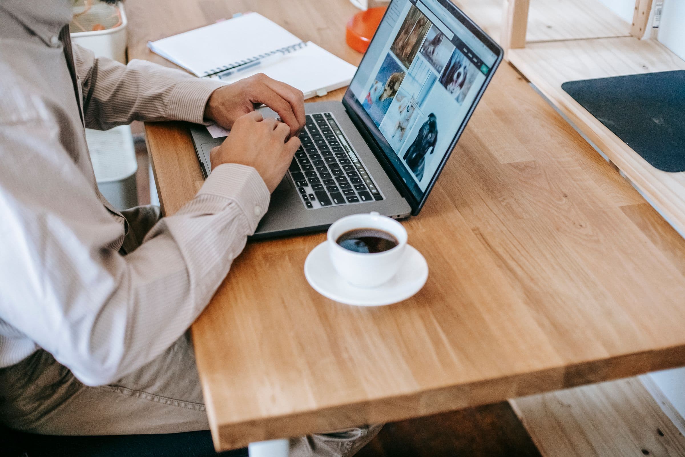 Person working on a laptop at a wooden desk next to a cup of coffee