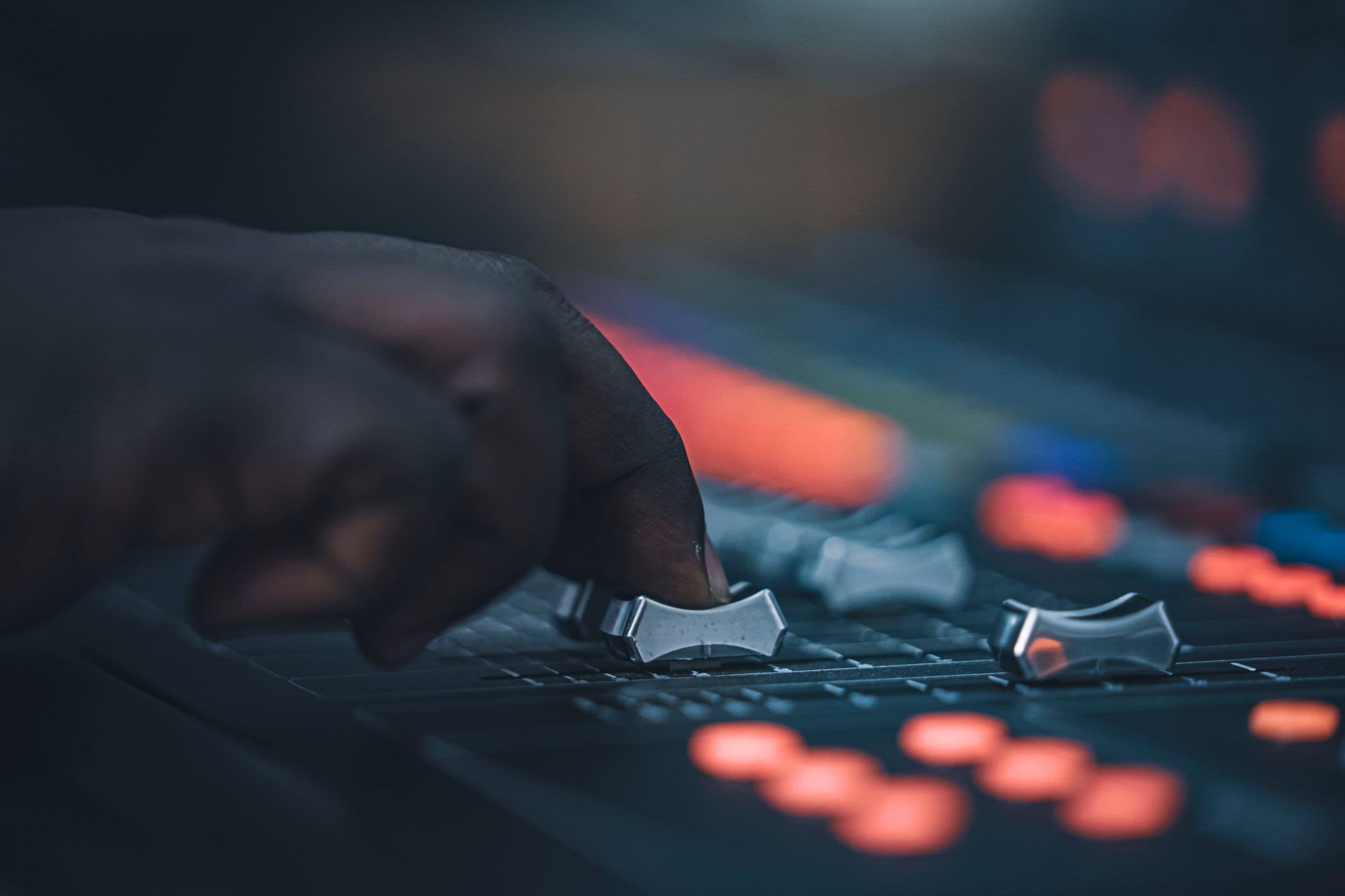 Hand moving a fader on a lit mixing console in a dark studio
