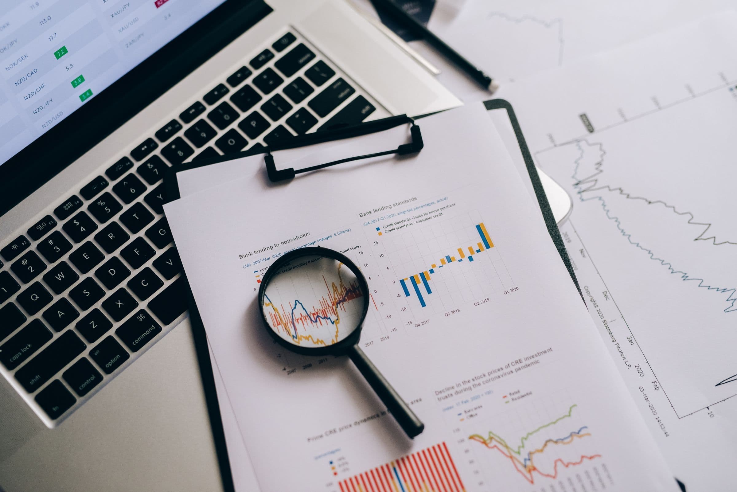 Magnifying glass over printed charts on a clipboard next to a laptop