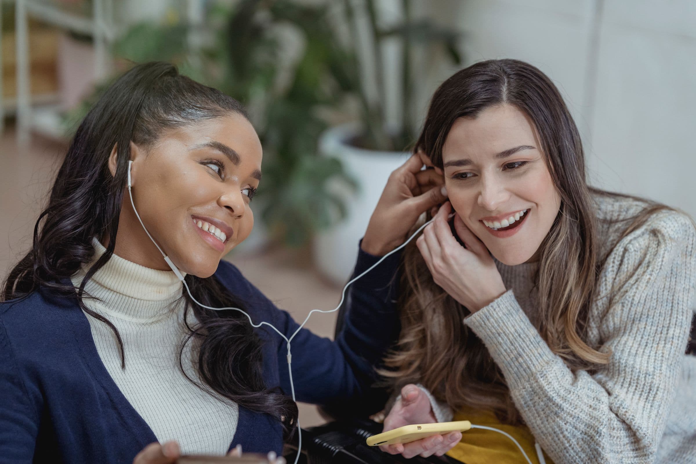 Two friends sharing earphones and laughing while listening to music on a phone