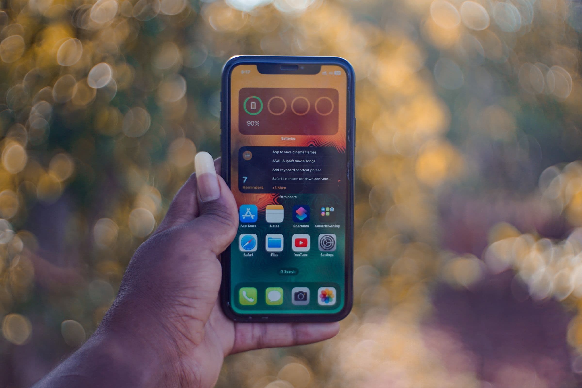 Hand holding up a smartphone against a blurred background of warm lights